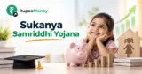Sukanya Samriddhi Yojana banner featuring an Indian girl, savings piggy bank, growing rupee coin stacks, education books, graduation cap, upward financial growth arrow, and RupeeMoney branding.