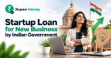 Startup loan for new business by Indian Government banner featuring a young Indian entrepreneur, laptop, business documents, rupee coins, growth arrow, startup idea illustration, Indian government building, and RupeeMoney branding.